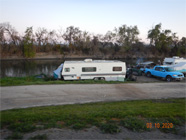 Image #1 Homeless encampment along the Sacramento River in Knights Landing. Pictured are several trailers, golf cart, truck, tents, boat with smoke coming up from an area in the background.