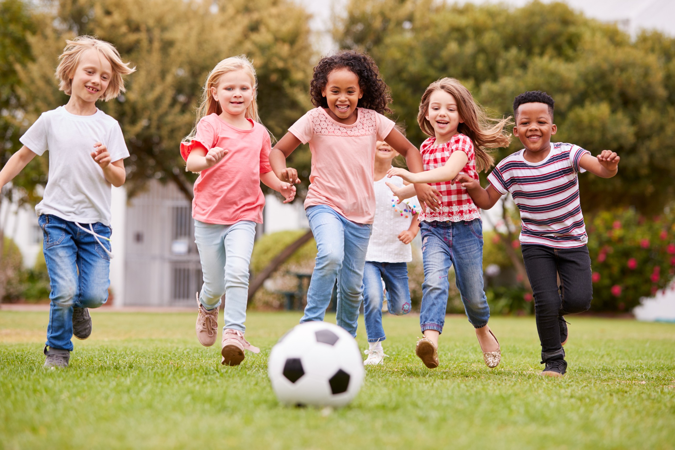 Five kids running towards a soccer ball