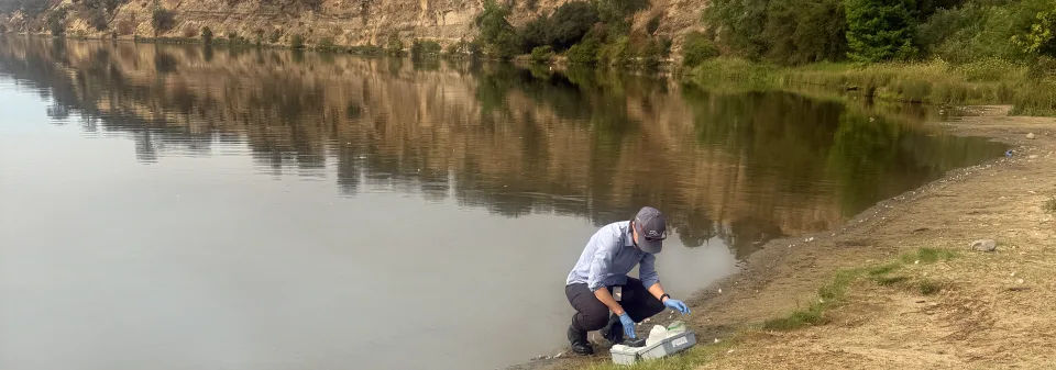 A scientist crouches with water monitoring equipment at the edge of Lake Natoma