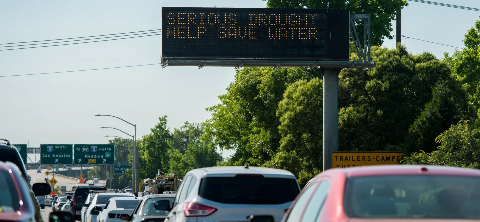 A photo of cars on a California highway with a Caltrans digital sign with the words &ldquo;SERIOUS DROUGHT HELP SAVE WATER&rdquo;