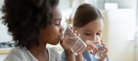 Two children drinking water from glasses