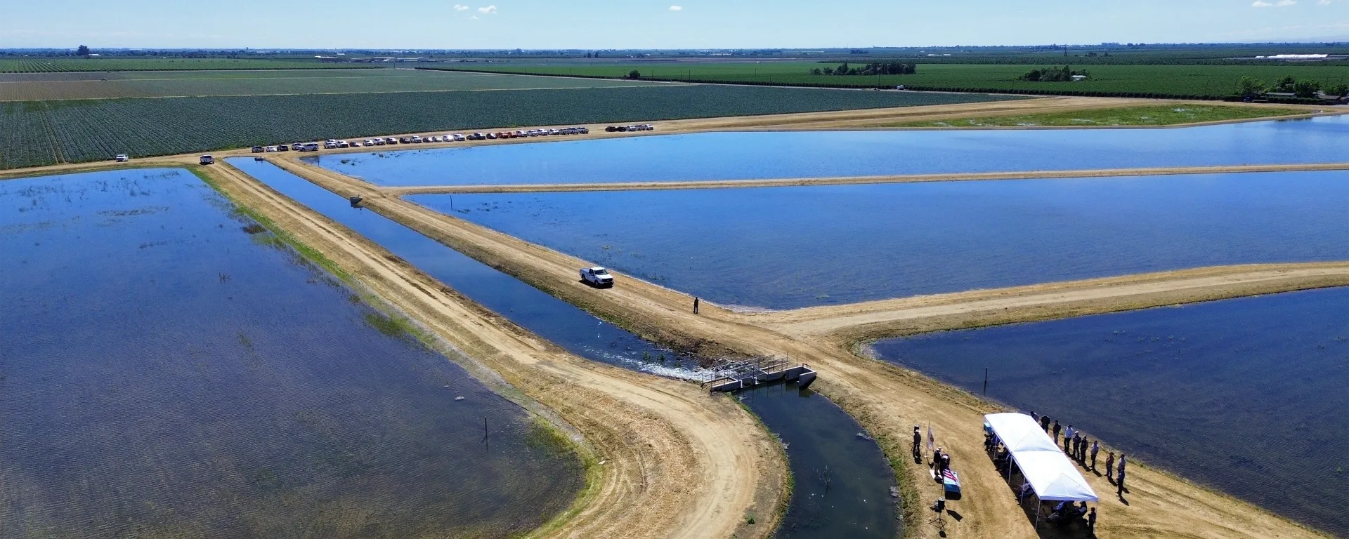 Four large ponds between raised dirt paths with an event tent surrounded by people at the Orestimba Recharge and Recovery project. Credit: Central California Irrigation District