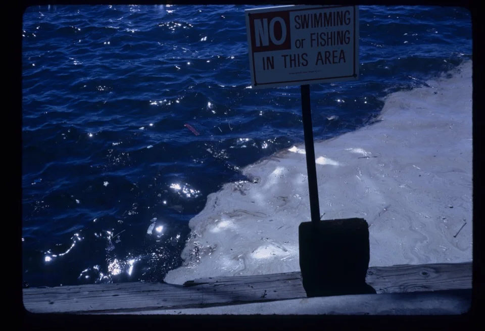 Oil sheen and a 'No Swimming or Fishing' sign near the Star of India, San Diego Bay, 1968